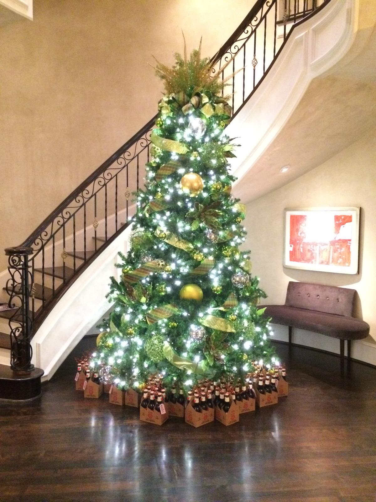A tall Christmas tree with gold ornaments beside a curved staircase