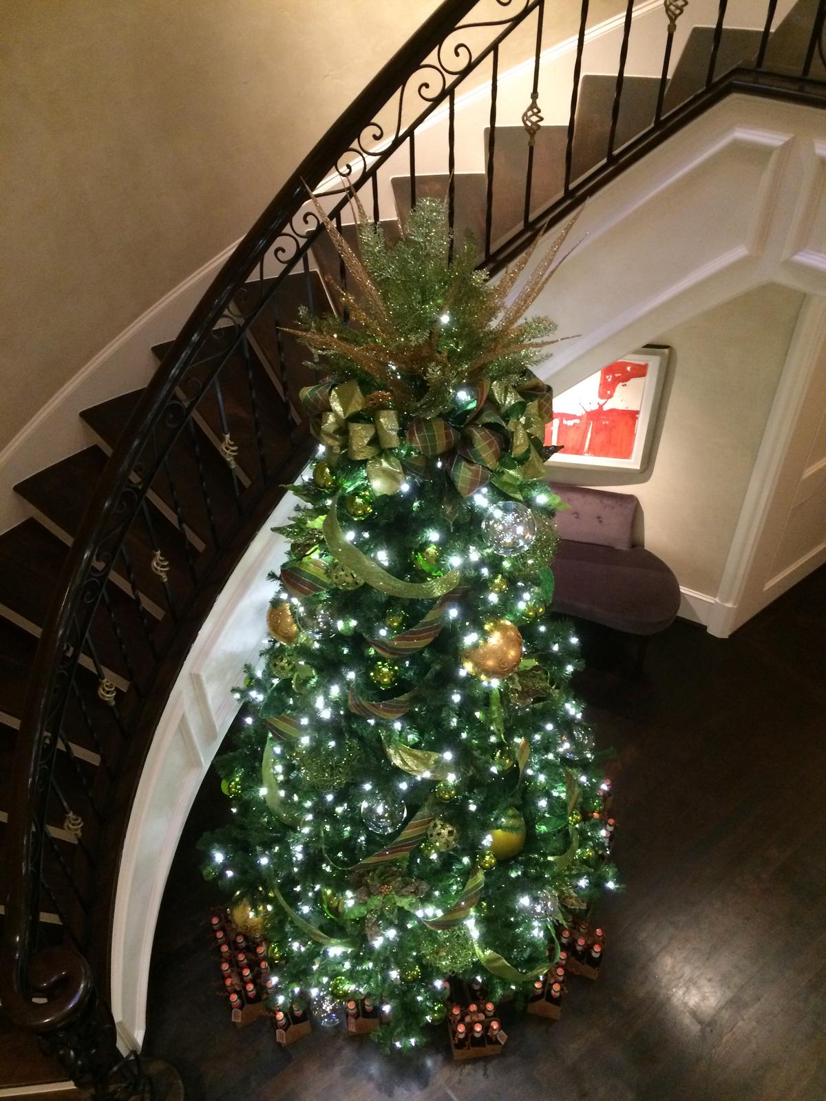 A tall Christmas tree with gold ornaments beside a curved staircase