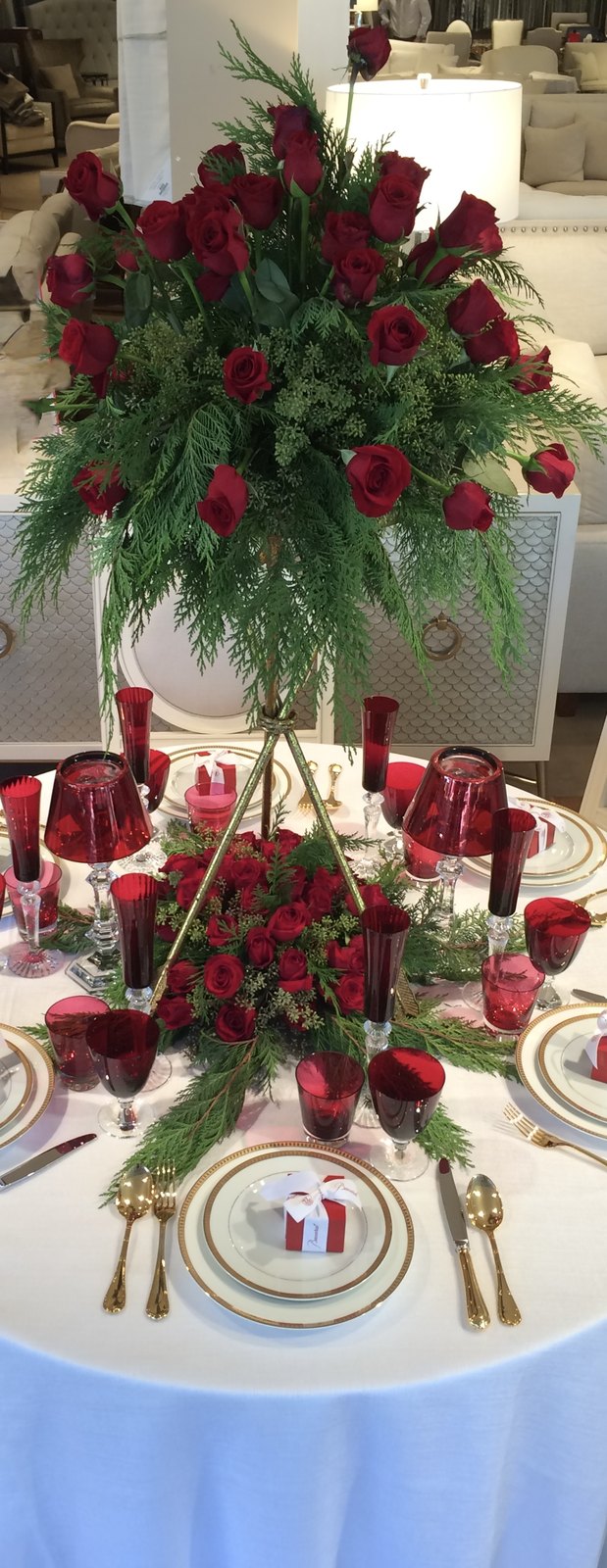 A round holiday table set with ruby glassware, red roses and gold-rimmed china
